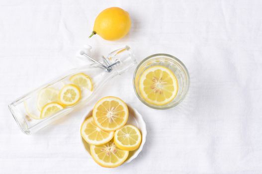 Top view of a glass of lemon water next to a swing bottle and whole piece of fruit. Horizontal format with copy space.