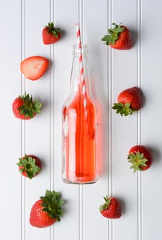 Strawberries surrounding a bottle of soda on a white bead board table. High angle shot in vertical format.