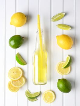 Limes and Lemons surrounding a bottle of soda on a white bead board table. High angle shot in vertical format.