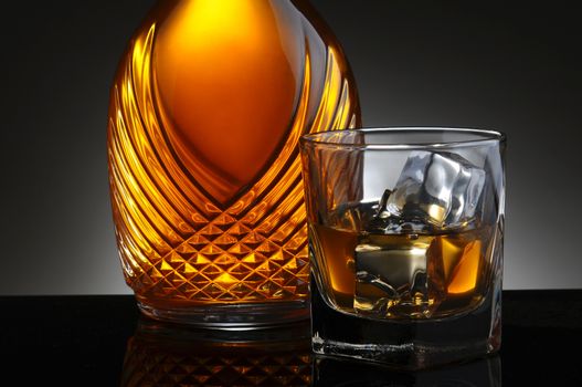 Closeup of an elegant decanter and a glass of scotch on the rocks. Horizontal format on a light to dark gray background.