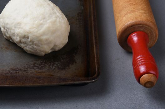 Closeup of a ball of raw bread dough on a baking sheet with a wood rolling pin.