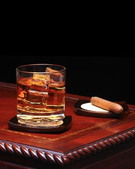 A glass of Whiskey with ice and cigar on a fancy table agains a black background with copy space. 