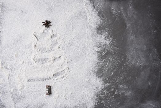 Christmas tree shape in flour spread out on a baking sheet. Tree topper is a star anise pod. 