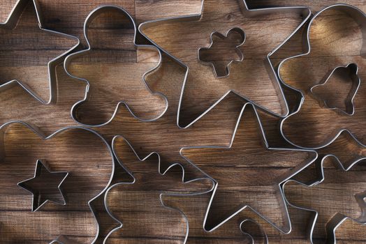 Closeup overhead viewof a group of assorted cookie cutters in various shapes on a wood kitchen table. Stars, gingerbread men, moose, bell and candy canes are shown. 