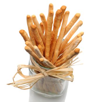Top view of bread sticks in a glass jar on a white background with reflection.  Jar is tied around the neck with rafia.