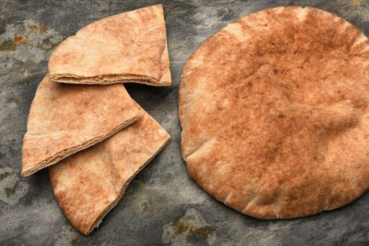 Top view of a loaf of Pita bread and three pita wedges on a slate table. 