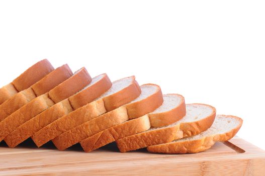 Closeup of fa loaf of white bread on a wood cutting board. Slices of bread are fanned out. Horizontal format over a white background.