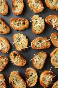 Closeup of a pan full of toasted garlic bread. The bread slices have parmesan cheese and other herbs and spices sprinkled on top. Vertical format shot from a high angle.