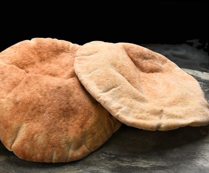 Closeup of loaves of whole wheat pita bread on a slate surface and black background.