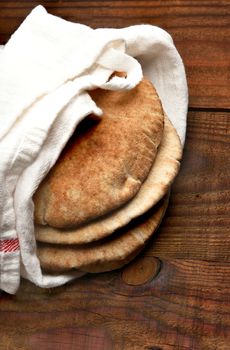 Whole wheat pita bread on a rustic wood table with copy space. The bread is wrapped in a towel and seen from a high angle. Vertical format.