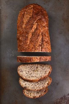 Top view of a loaf of multi-grain bread on a baking sheet. The loaf is partially sliced, 