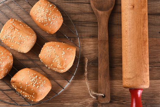 Overhead view of a rack of Sesame seed dinner rolls next to a wooden spatula and rolling pin. 