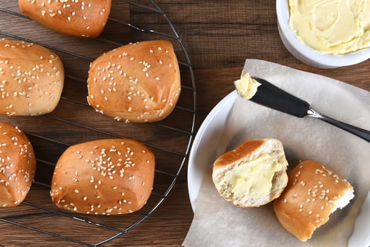 High angle view of sesame dinner rolls on a wire rack, with bread plate, and butter crock and knife.