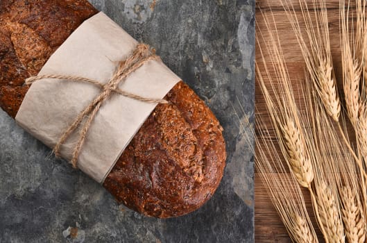 Top view of a loaf of multi-grain bread on a slate surface and wheat stalks.