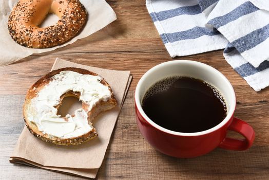 A fresh cup of coffee and a bagel with cream cheese on a wood table. 