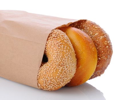 Closeup of three bagels in a brown paper bag laying on its side. Horizontal format on white with reflection.