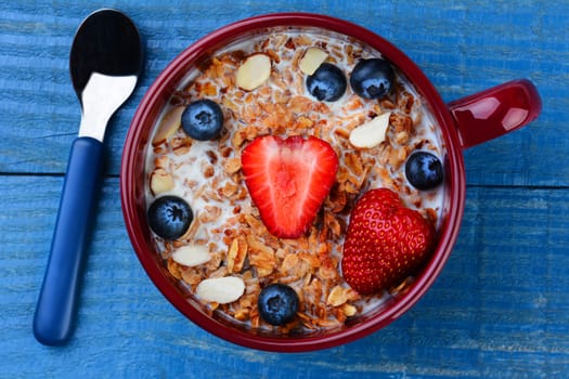 High angle photo of a large mug filled with a healthy whole grain cereal and fruit. Strawberries, blueberries and sliced almonds on a rustic painted kitchen table. Vertical format but works as a horizontal also.