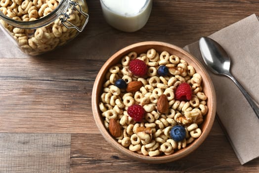 High angle view of a bowl of breakfast cereal with blueberries, raspberries and nuts. A bottle of milk and spoon are also on the rustic wood table, with copy space.