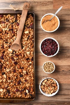 High angle view of fresh homemade granola. Baking sheet filled with the tasty, healthful food with containers of ingredients.