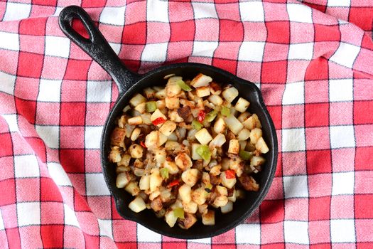 High angle shot of a cast iron skillet with potatoes O'brien on a red checked table cloth.