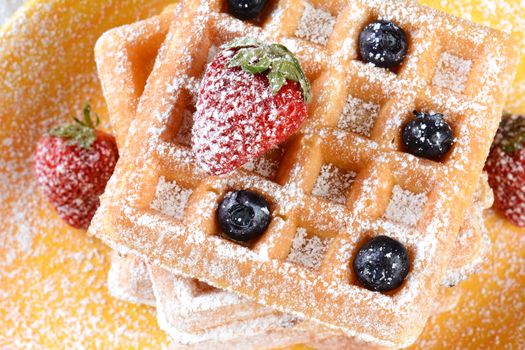 Closeup of fruity waffles covered with powdered sugar. Fresh blueberries and strawberries on a stack of Belgian style waffles. Horizontal format.