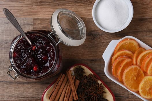 Homemade Cranberry Sauce with Orange Slices spices and sugar bowl on a wood table.