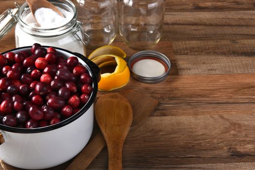 A pot of fresh cranberries surrounded by empty canning jars and bowl of sugar and utensils. Horizontal format with copy space.