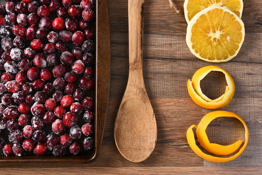 A kitchen sheet of sugared cranberries with wooden spoon and orange peel and slices. Preparation for making Thanksgiving cranberry sauce.