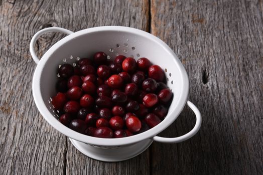 High angle view of a colander with fresh cranberries on a rustic wood table. 