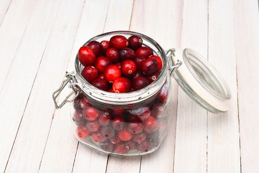 A canning jar filled with fresh whole cranberries on a white rustic kitchen table, the jar is open and misted with water.