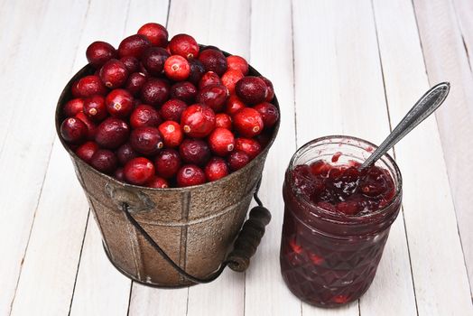 A bucket of fresh picked cranberries and a jar with the sauce made form the berries. 