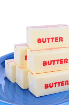 Closeup of sticks of wrapped butter on a blue plate. Vertical format over a white background.