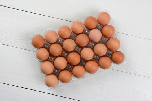 High angle shot of a 24 pack of organic brown eggs on a rustic white wood table. Horizontal format with copy space.