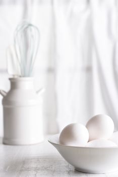High Key Egg Still Life: Fresh eggs in a white bowl in front of a window with white curtains. Vertical orientation.