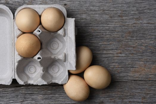 A carton of fresh eggs three eggs in the carton and three on the rustic wood table. Horizontal with copy space.