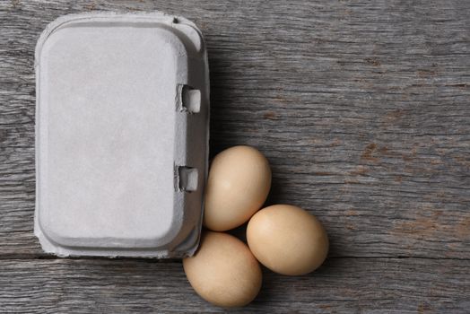 A Carton of fresh eggs with three on the rustic wood table. Horizontal with copy space.