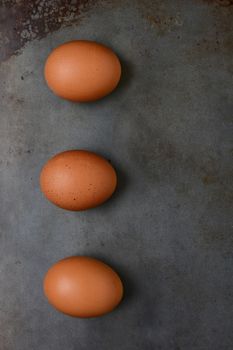 Overhead shot of three organic brown eggs on a metal baking sheet. Vertical format with copy space.