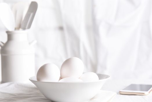 High Key Egg Still Life: Fresh eggs in a white bowl in front of a window with white curtains. Horizontal orientation.