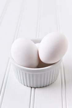 Egg White on White Still Life. Eggs in a ramekin on a white table. Vertical format with copy space.