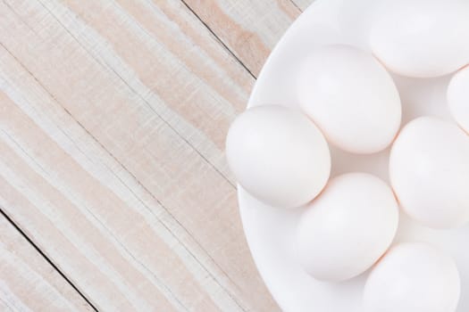 High angle view of a white bowl filled with white eggs on a white wooden rustic kitchen table. Horizontal format with copy space.