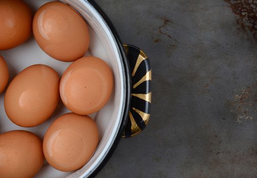 Overhead shot of brown eggs in pot of water. Closeup only half the pot is showing on a well used cooking surface.