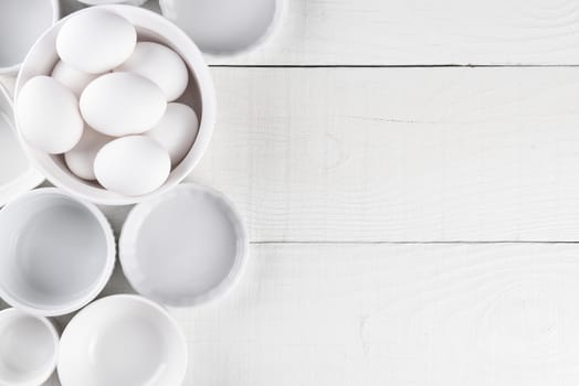 White Ramekins on White Wood Table with copy space. One dish is filled with eggs.