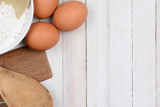 High angle shot of a baking still life, The objects, flour bowl, brown eggs and wood utensils are in the upper left corner and side, leaving plenty of copy space.