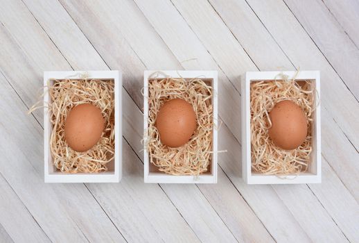 Three brown eggs in wood crates on a whitewashed wood surface. High angle shot in horizontal format. 