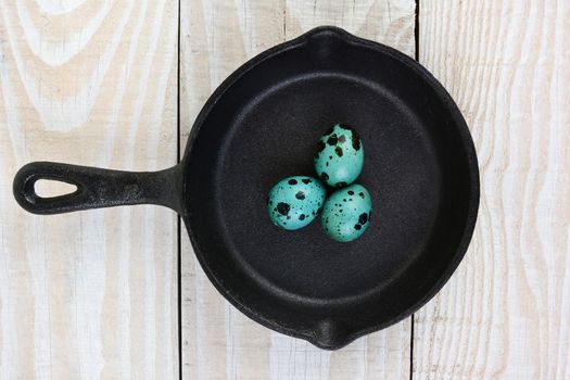 High angle shot of a cast iron frying pan  with three blue speckled eggs. Horizontal format on a rustic wooden farmhouse style table.