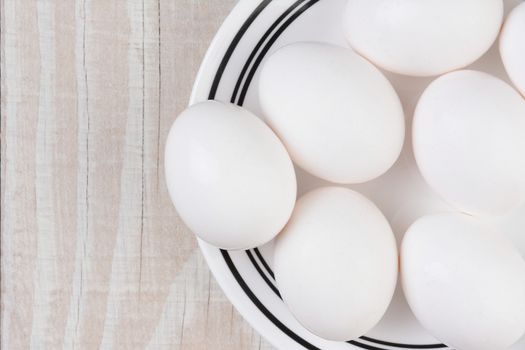 White eggs on a white plate with black trim on a rustic whitewashed table. Horizontal format with copy space.