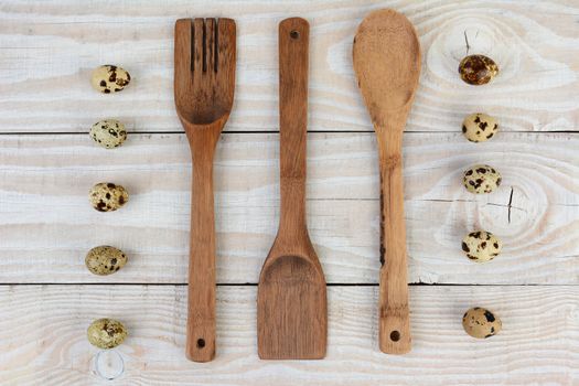 High angle shot of wooden utensils and two lines of quail eggs. Horizontal format on a rustic farmhouse style table.