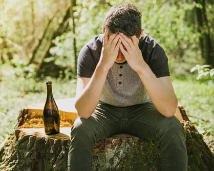 An unhappy man solves problems with alcohol. sad and alone with a bottle of alcohol in nature.