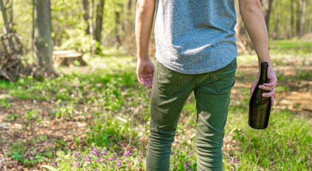 man with a bottle of alcohol in the woods. Solving the problem of drunkenness and loneliness.