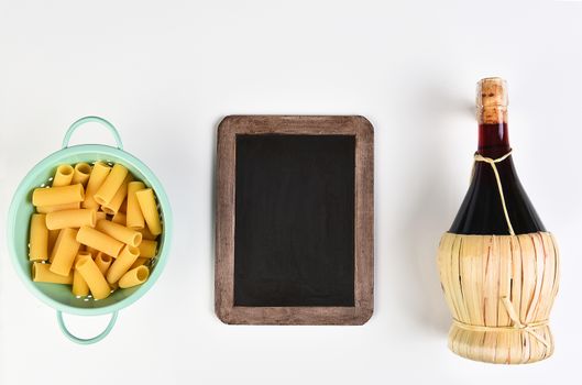 Top view of a blank chalkboard with a colander filled with rigatoni pasta and a bottle of Chianti wine. Horizontal format on white.